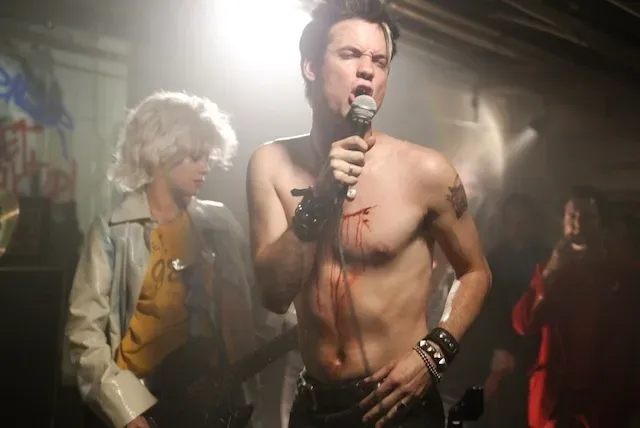 Punkowy koncert w podziemnym klubie, wokalista z mikrofonem i gitarzysta w tle.