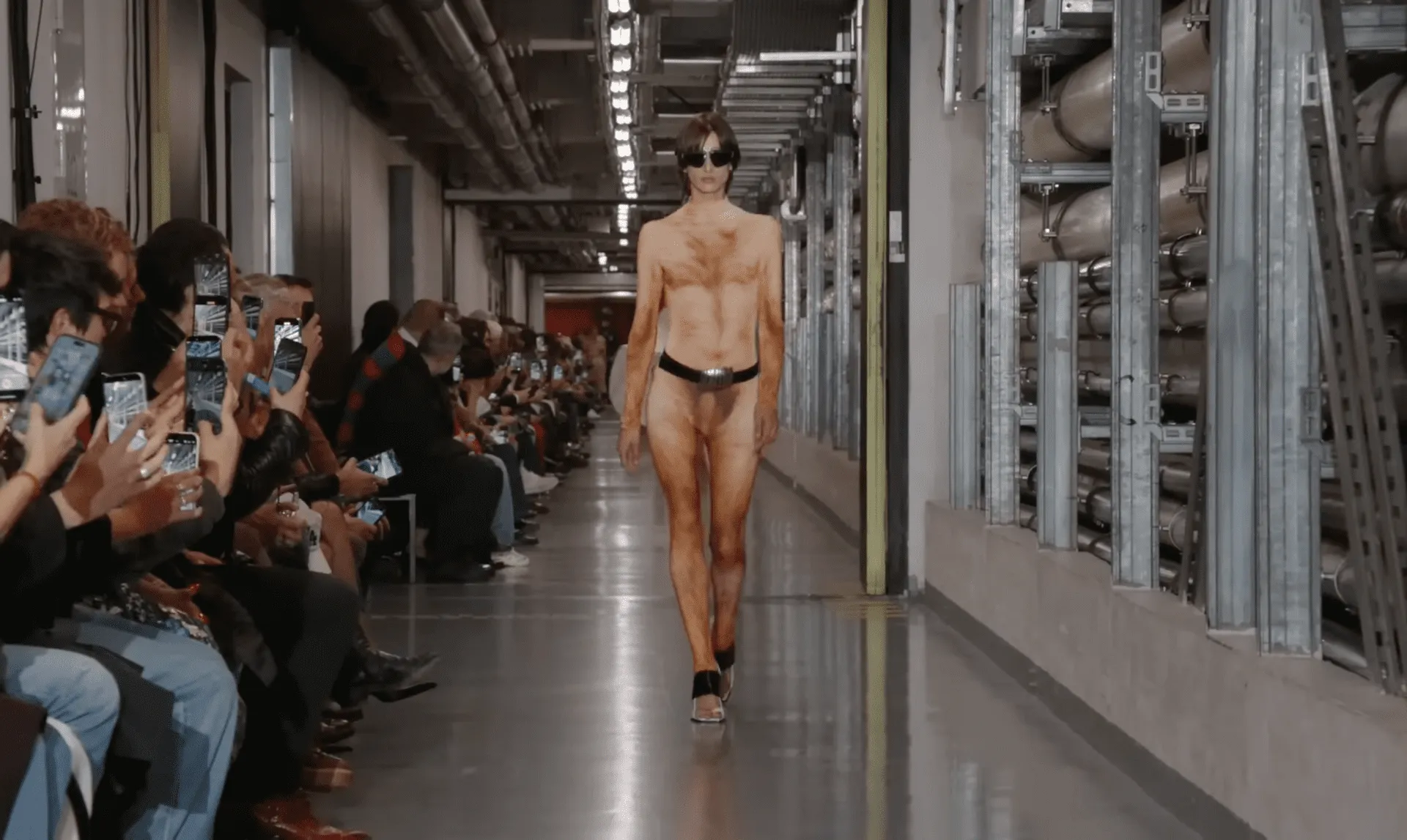 Model na wybiegu w farbie brązowej, prezentujący odważną stylizację.
