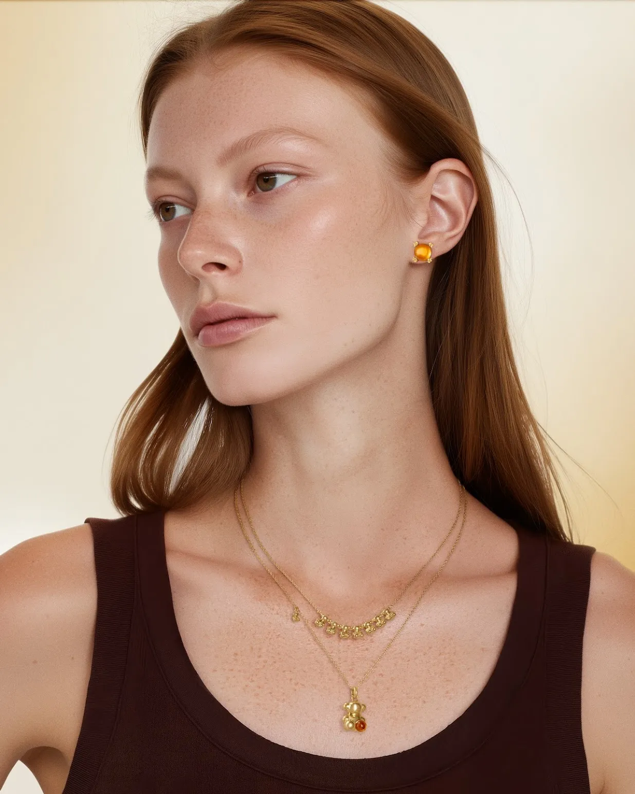 Młoda kobieta z rudymi włosami, w złotych biżuterii na tle beżowym.