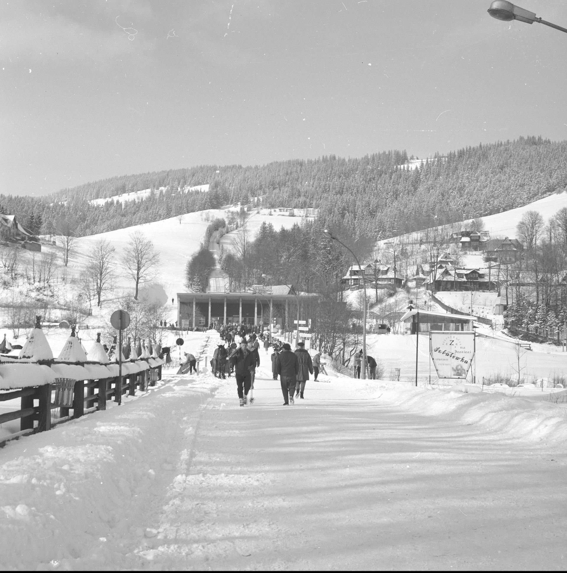 Turyści na deptaku pod Gubałówką. W tle dolna stacja kolejki linowo-terenowej i pasmo Gubałówki.