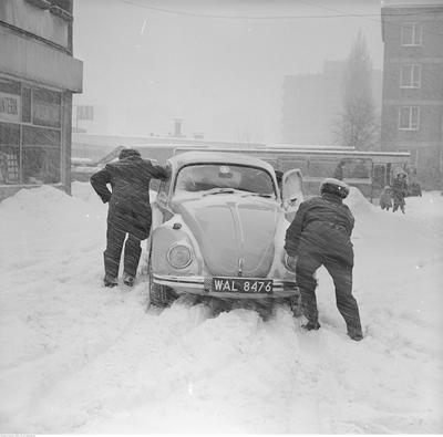 Mężczyźni pchający samochód Volkswagen Garbus. Z lewej budynek przy ul. Malczewskiego 48/50.