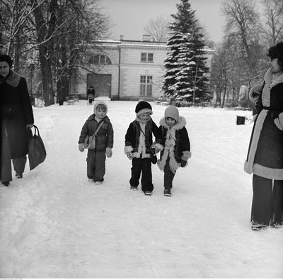 Dzieci z rodzicami na spacerze. W tle fragment Pałacu Na Wodzie.